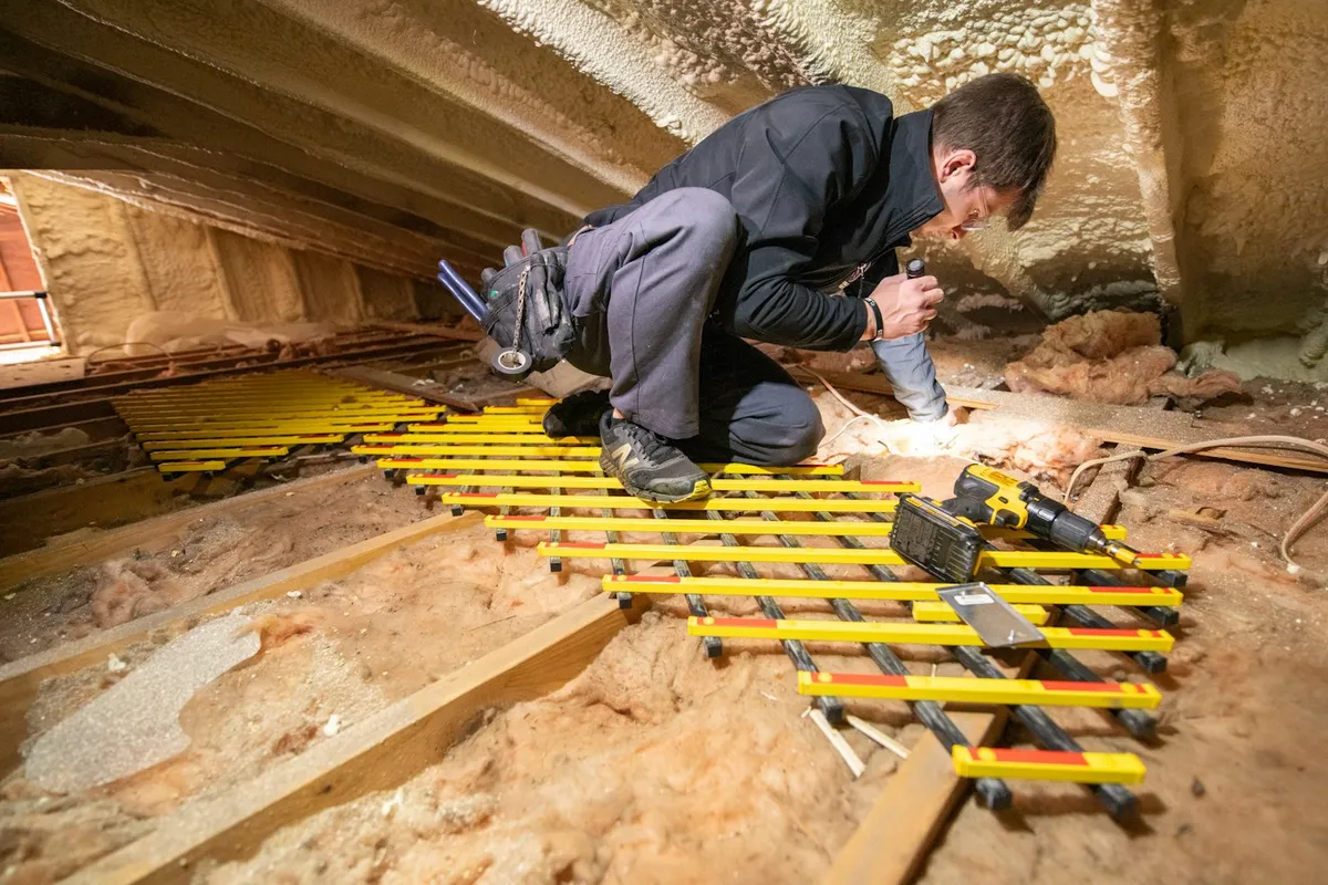 A person working in a dark attic space between roof timbers