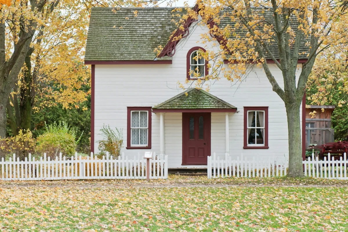 A white house framed by maple trees turning orange and red on an autumn day