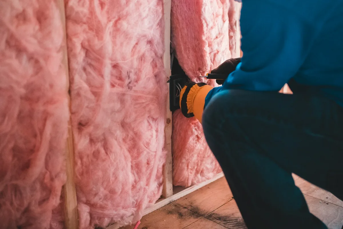 Pink fibreglass batt insulation in a stud wall with electrical wiring run through it