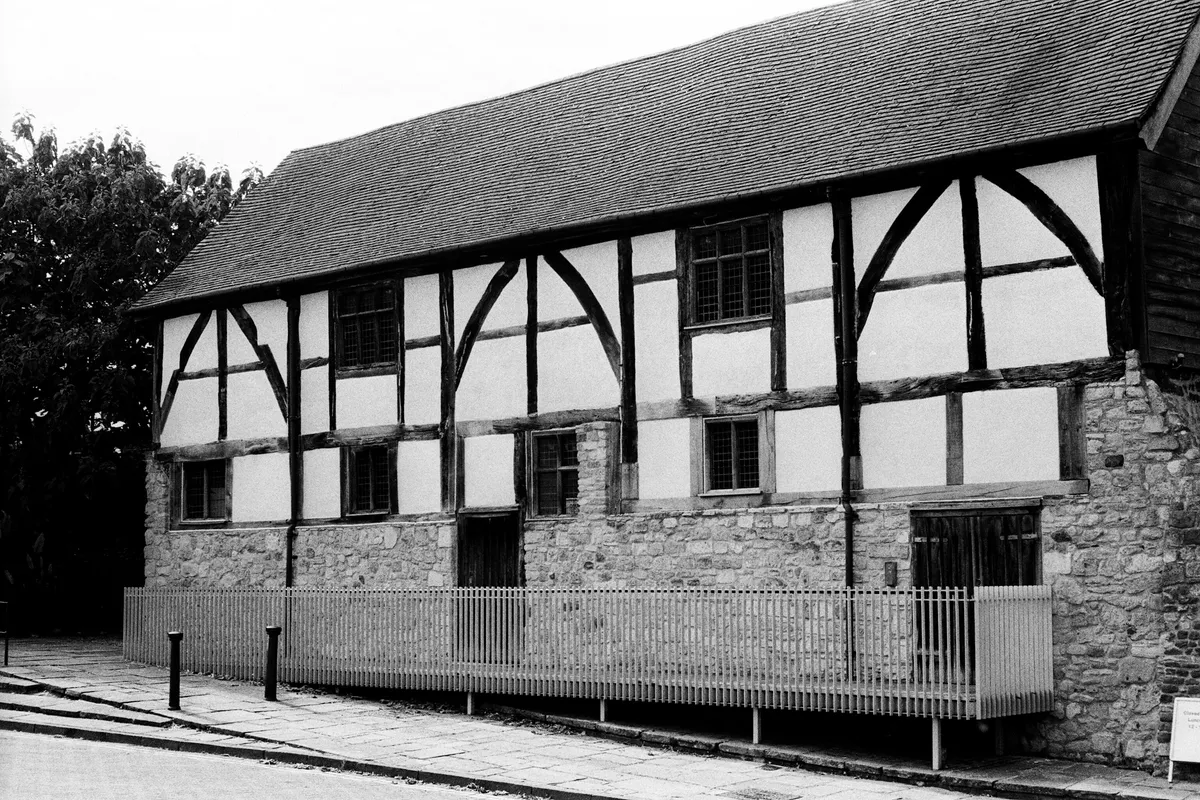 A timber-framed building sitting on an old stone base, in black and white