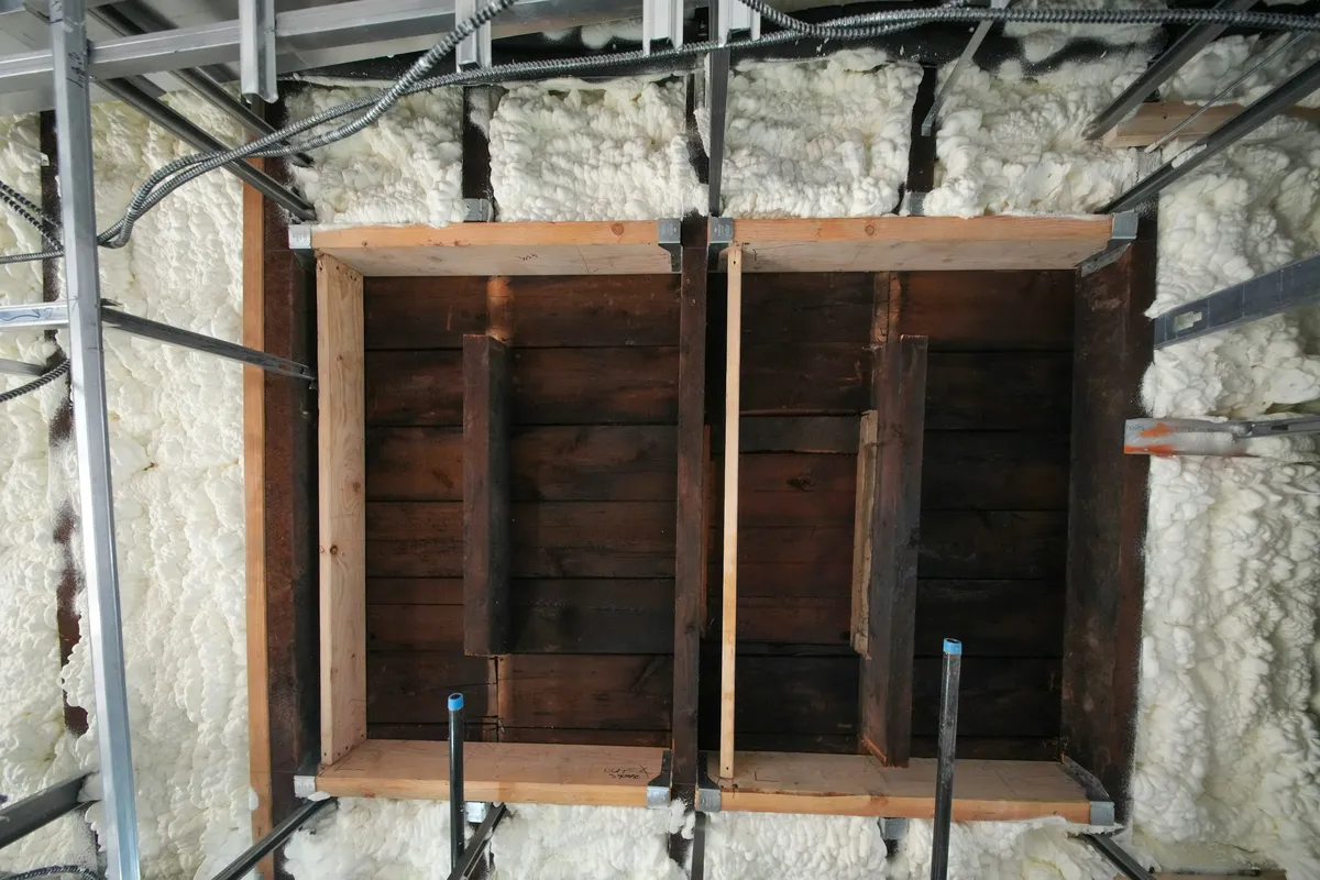 Closed-cell spray foam insulation filling the bays around old timber boards and metal framing
