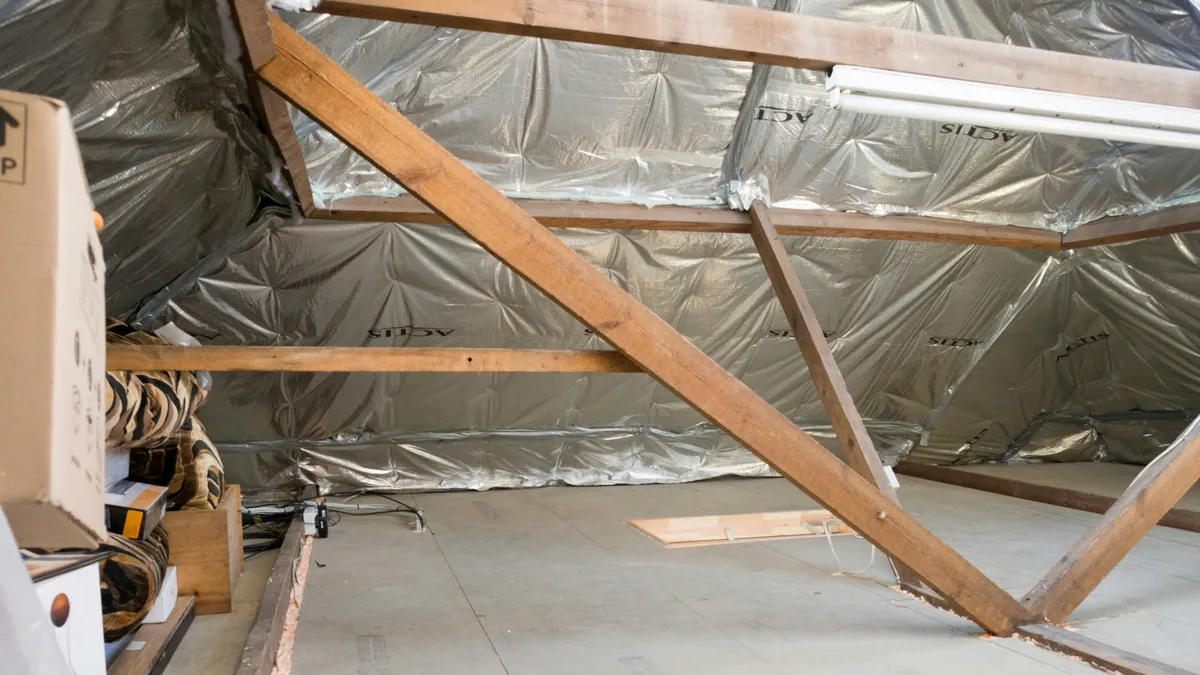 Attic under a pitched roof with exposed timber trusses and silver foil-faced insulation