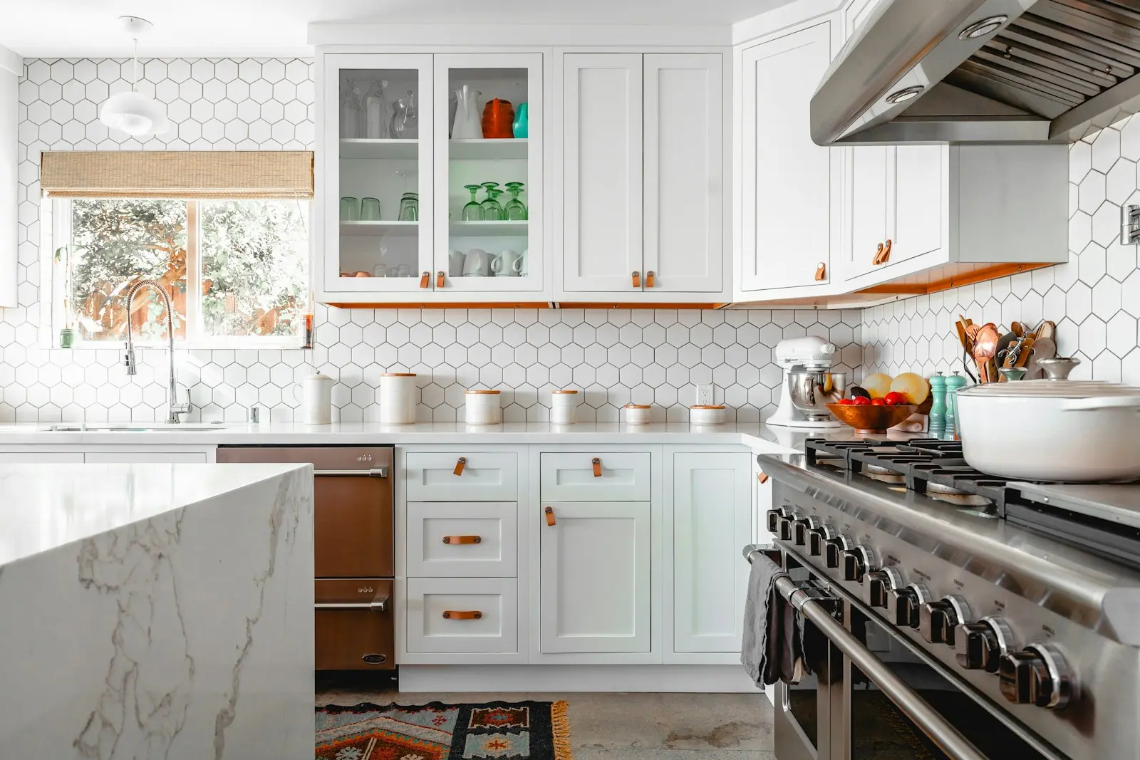 A bright kitchen with white cabinets, hexagonal wall tiles and a marble island