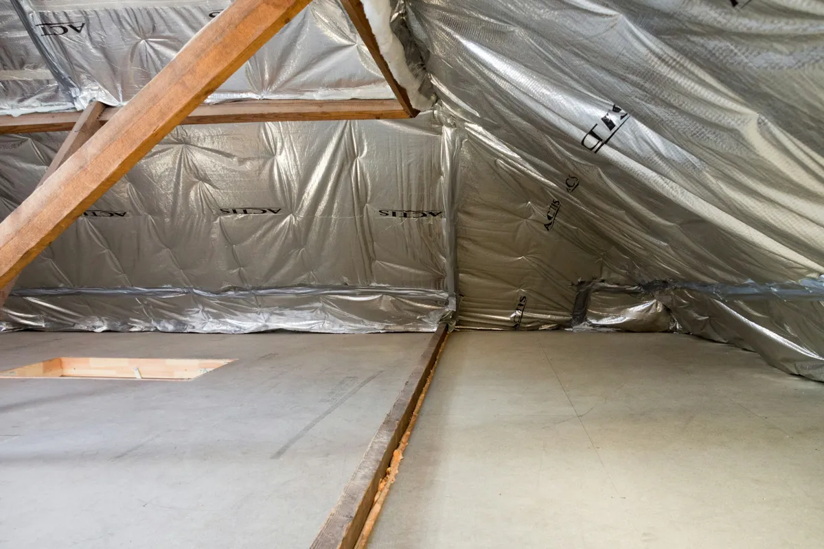 Insulation laid between wooden roof beams inside an unfinished attic space