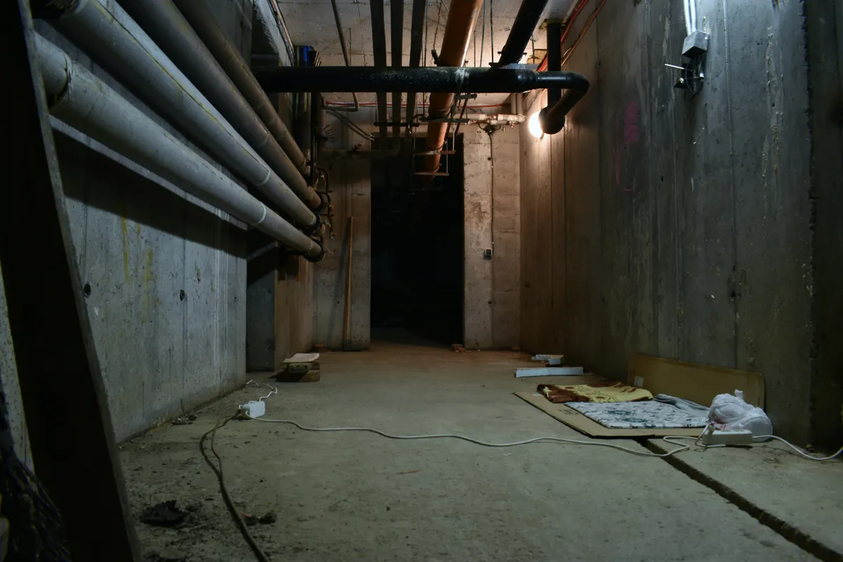 Dark basement room with exposed overhead pipes and a bare floor