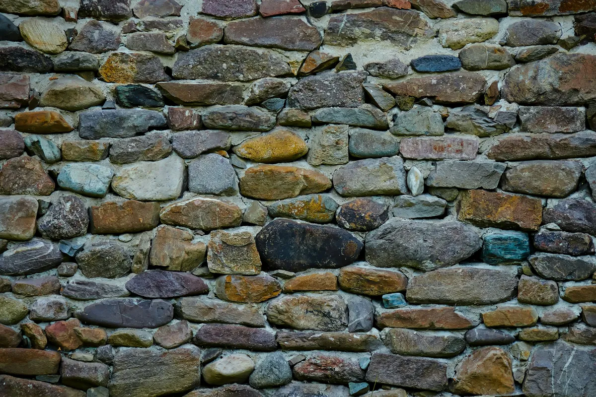 A rough stone wall built from irregular rocks with a barred opening