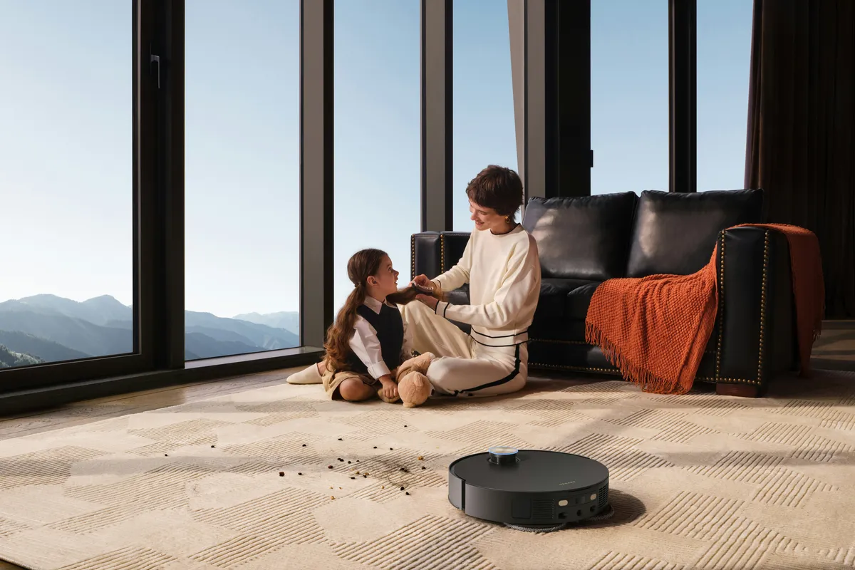 Adult and child sitting on a patterned carpet beside a round robot vacuum