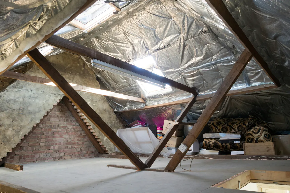 Open attic floor between timber trusses with foil-faced insulation overhead and stored boxes