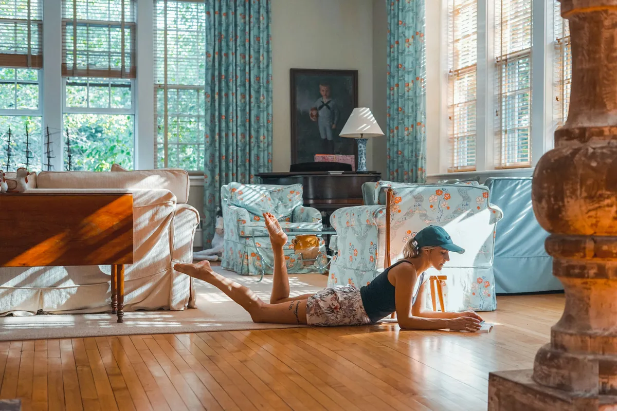 Person lying on a bare floor beside a sofa in a bright room