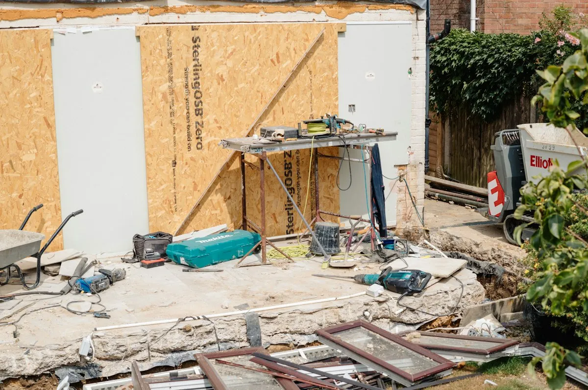 Renovation site outside an older home with tools and materials scattered