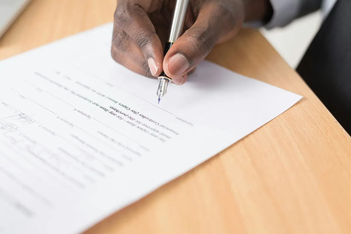 Person writing on a printed agreement at a desk