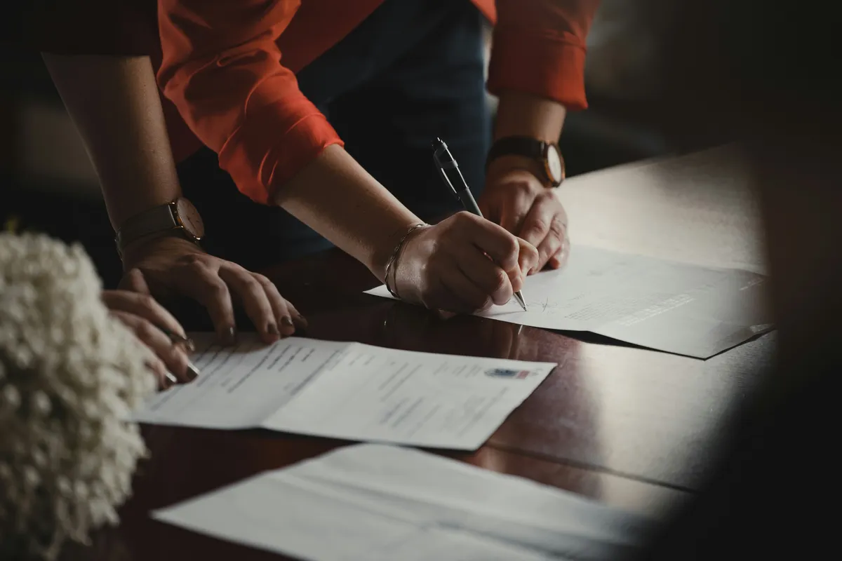 Two people signing paperwork across a desk