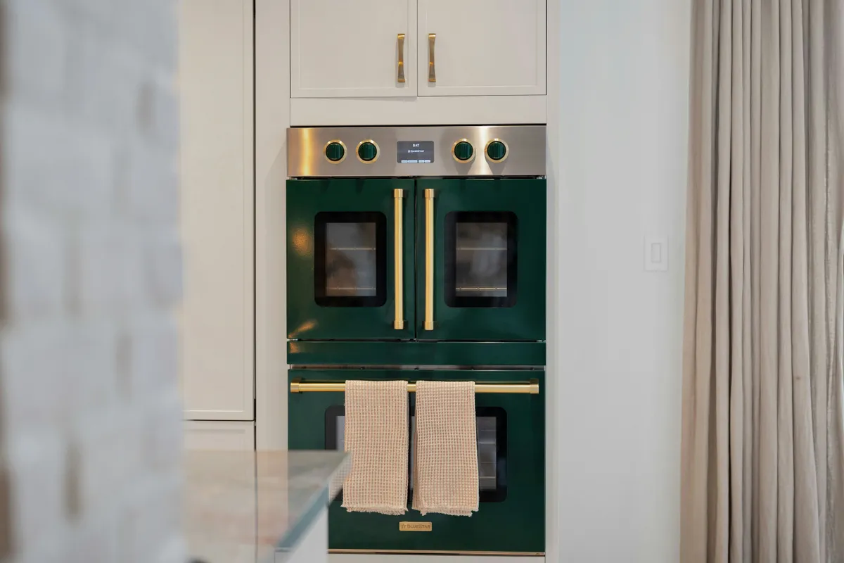Dark green double oven built into cabinetry with brass handles