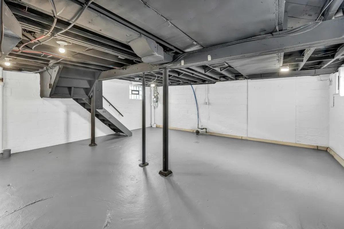 Unfinished basement with exposed joists, support posts and a staircase
