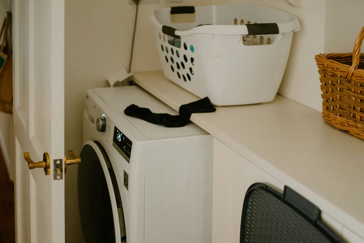 White washing machine with a laundry basket and a stray sock