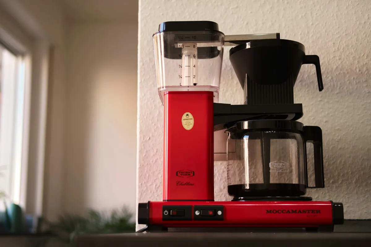 A red drip coffee maker with glass carafe on a kitchen worktop