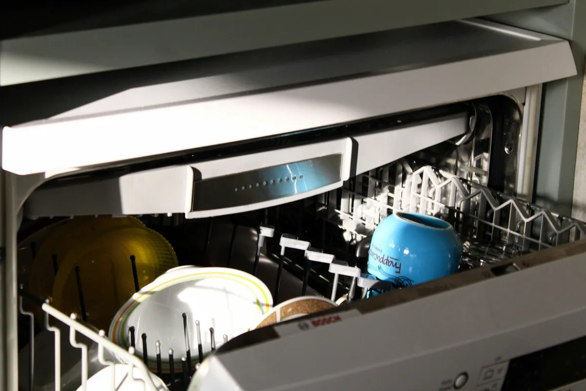 An open dishwasher with plates and a blue mug loaded on the racks
