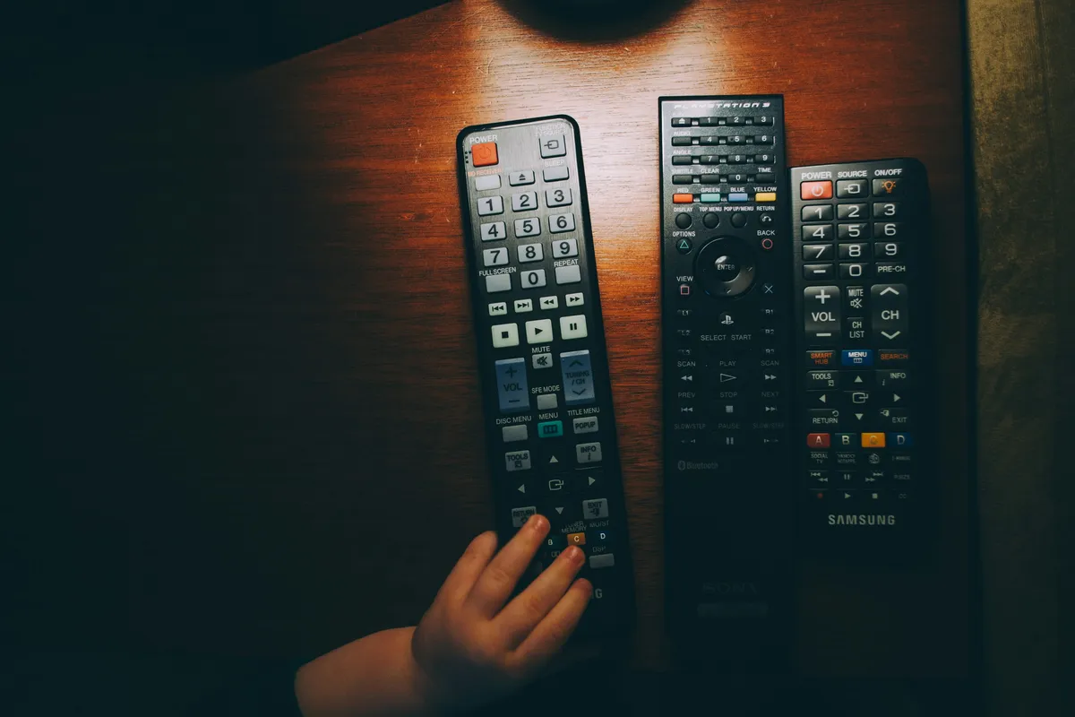 Three black remote controls lying on a wooden table